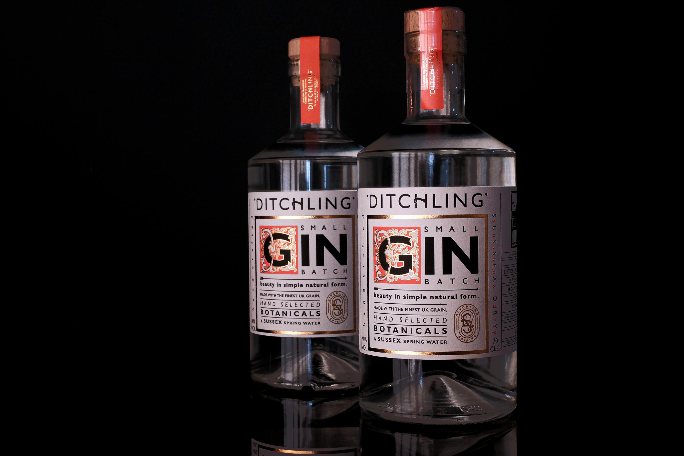 Two bottles of Ditchling gin one behind the other, standing in front of a dark background