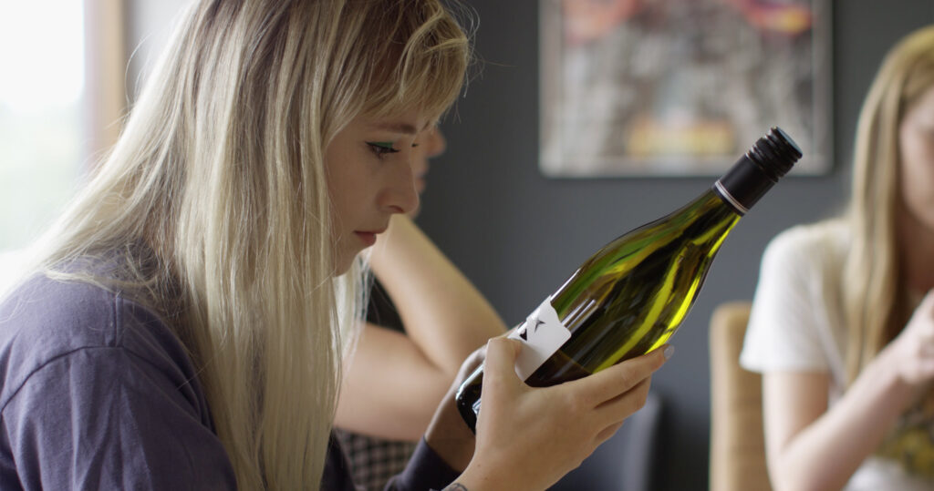 Female with long blond hair looking at the label of a green bottle of wine