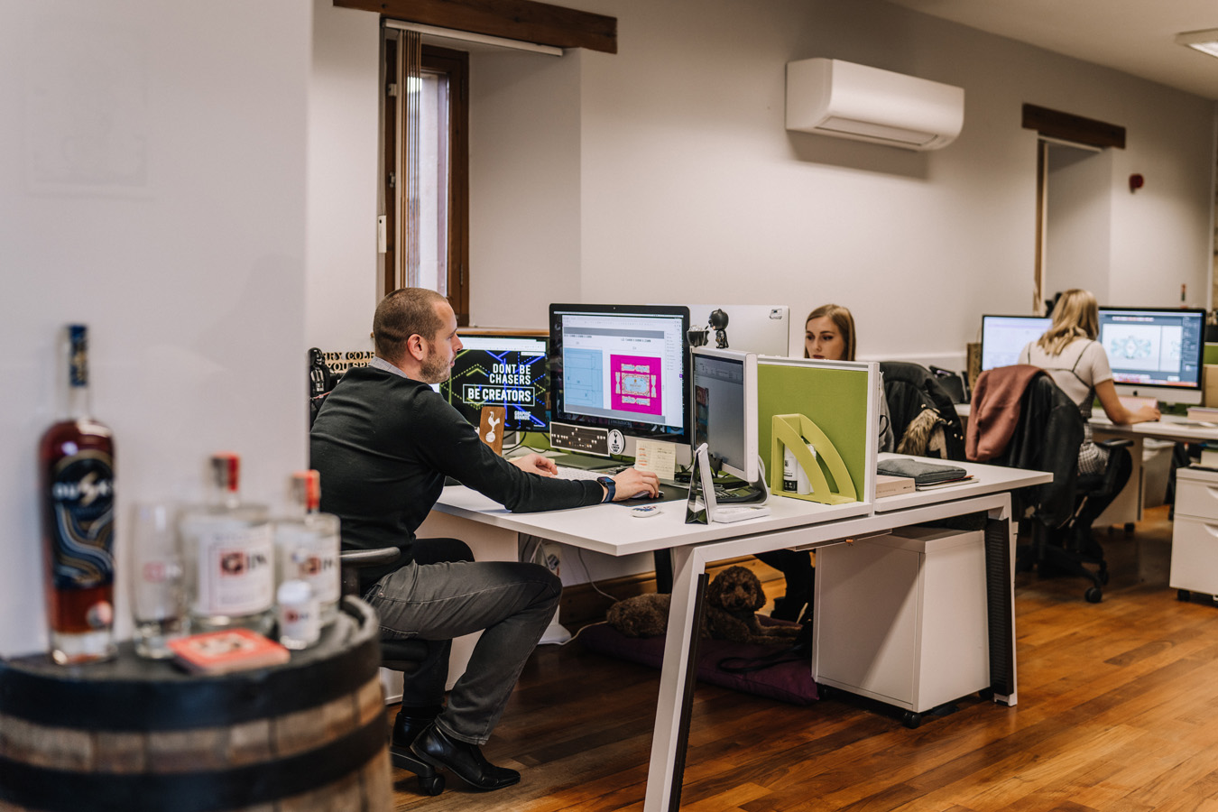 The people sat in an office at their desks, one behind another, each looking at their computer screens