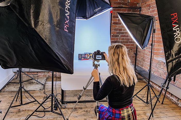 Photographic studio set up with flash lights and a female crouched down taking photos of a box