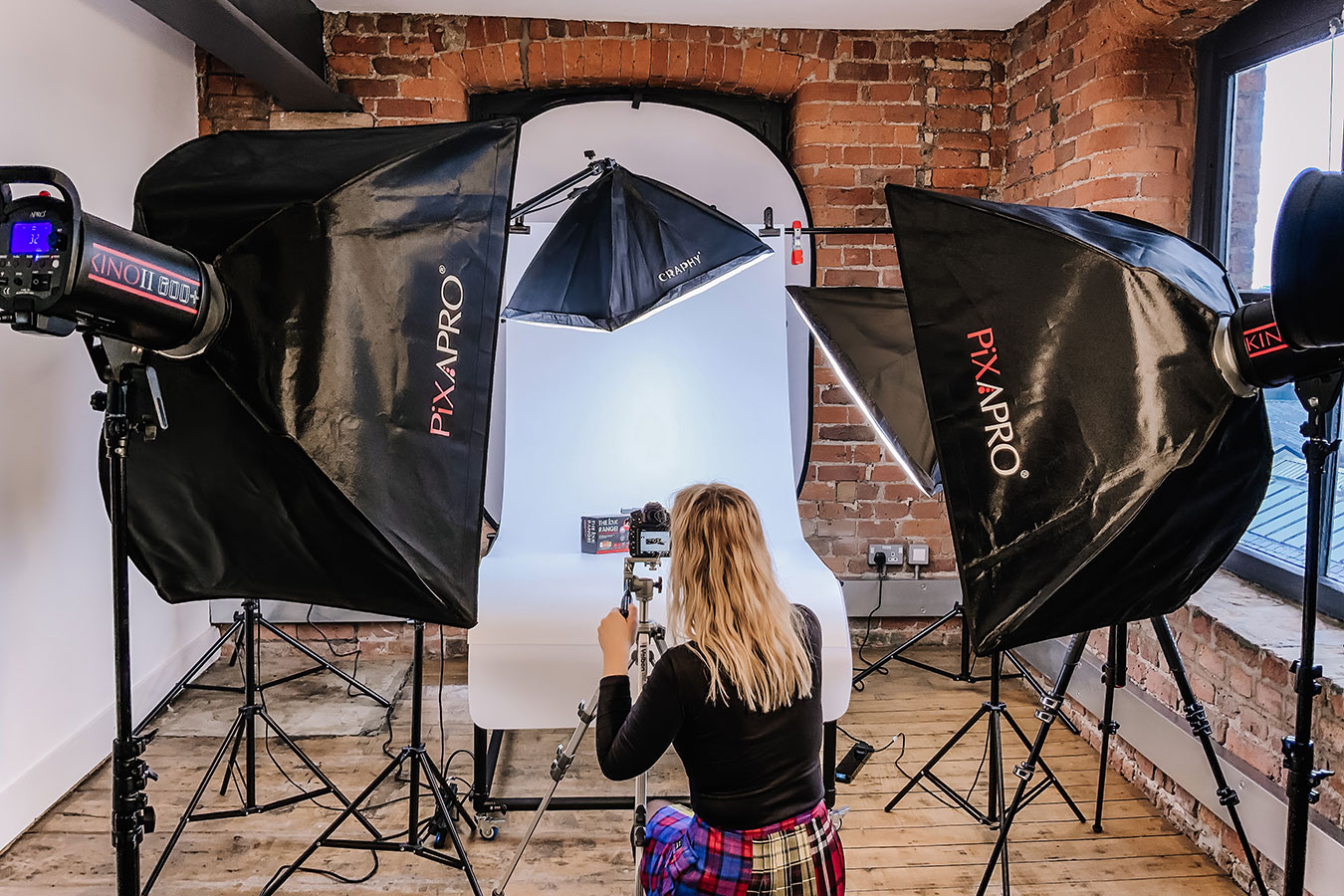 Photographic studio set up with flash lights and a female crouched down taking photos of a box