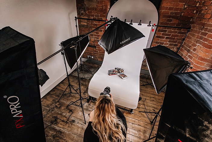 Top down view of a photographic studio set up with flash lights and a female crouched down taking photos of a box