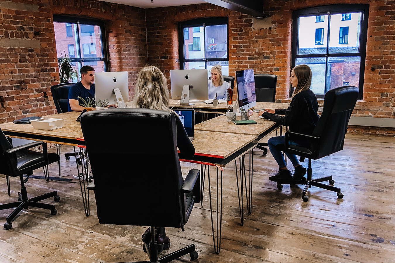 Four people sitting around a desk in an office with large sash windows and exposed brickwork