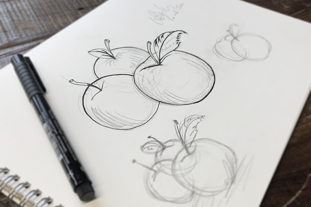 Pencil and pen drawings of apples on a white drawing pad