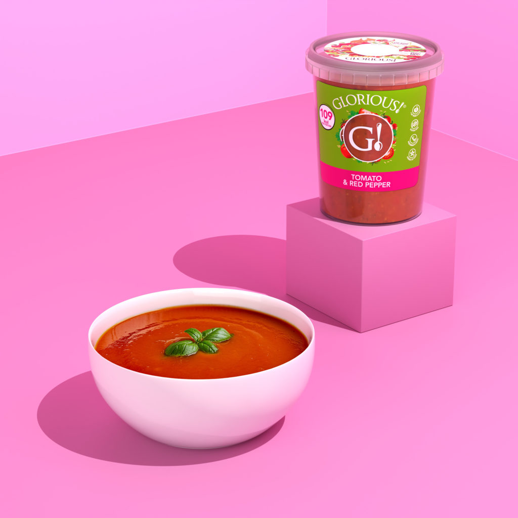 Pot of Glorious Soup in the tomato and red pepper flavour on a box, with a pink background and a white bowl of soup decorated with basil leaves
