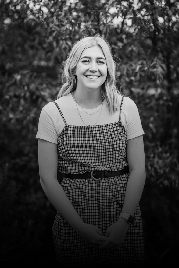 Smiling female wearing a white t-shirt and a checked dress standing in front of a tree with red leaves